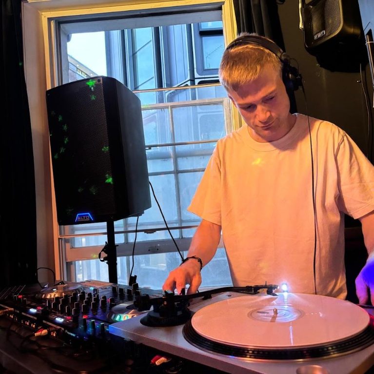A DJ cueing a record on the turntable by the window